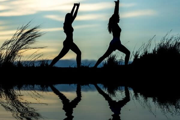 Sagome di donne in posizione yoga al tramonto sul lago:  lo yoga aiuta a capire le cause dello stress