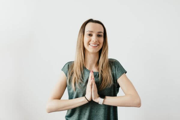 Ragazza sorridente in piedi con le mani in namastè a simboleggiare la gioia che deriva dallo yoga e dal suo potere terapeutico alternativo