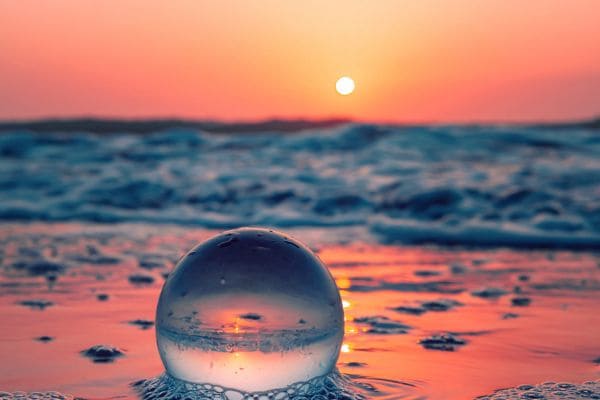 Bolla d'acqua sul bagnasciuga in cui si specchiano il mare e il sole al tramonto a simboleggiare l'unione di filosofia e scienza