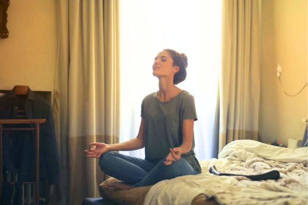 Donna seduta sul letto con occhi chiusi: come fare meditazione