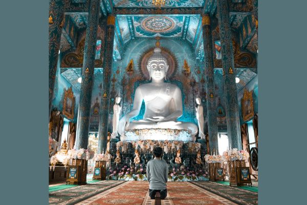 Uomo seduto in ginocchio davanti a una grande statua del Buddha a simbolo della Vipassana Meditazione